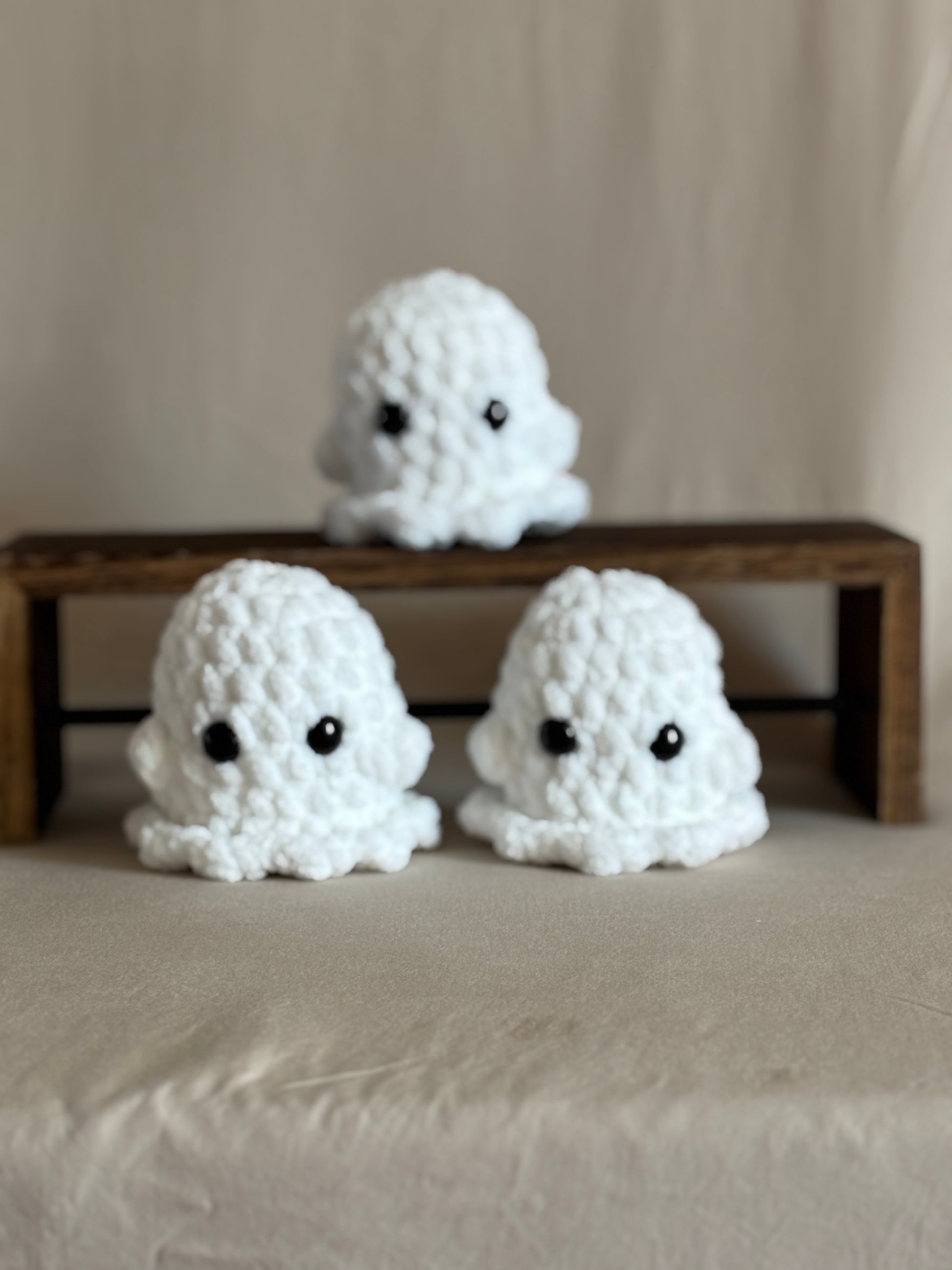 Three white crochet ghosts on a neutral background