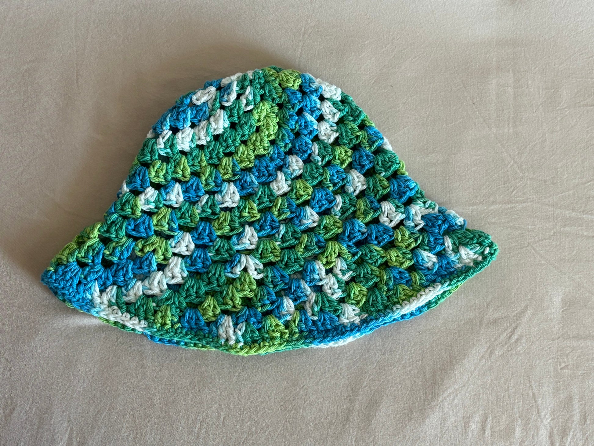 Crocheted hat with a wavy pattern in blue, green, and white on a beige surface