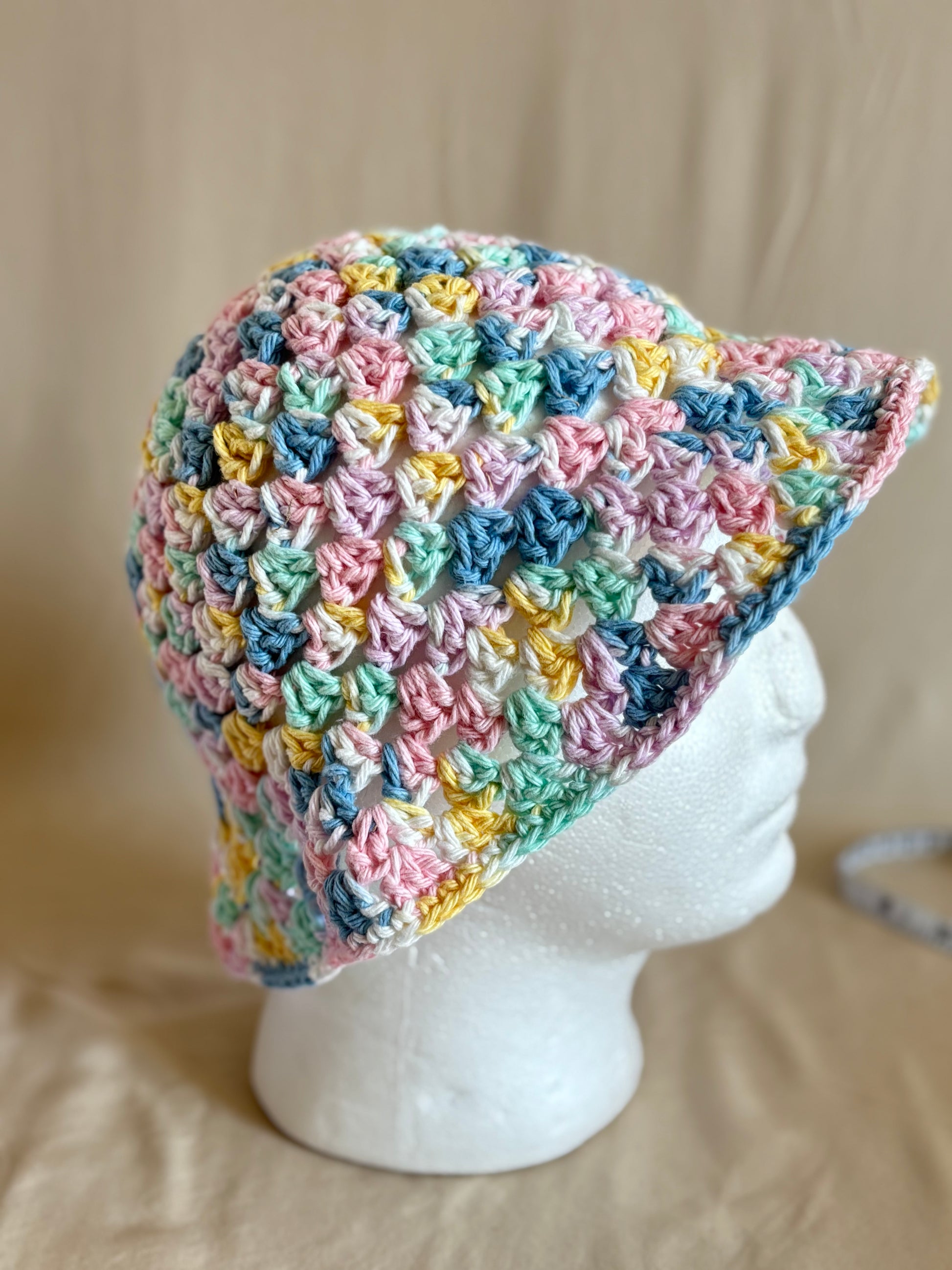 Multicolored crochet bucket hat on a mannequin head against a beige background