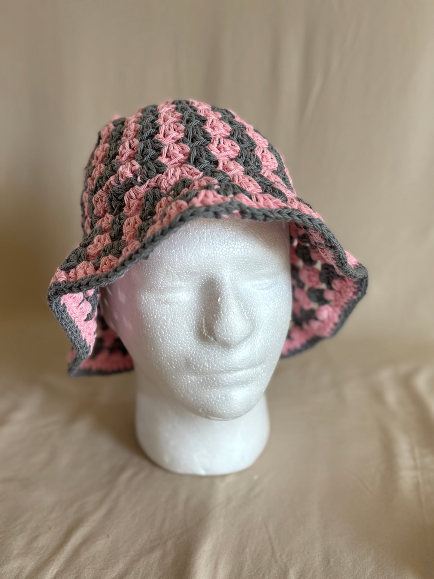 Pink and gray crocheted hat on a mannequin head against a beige background
